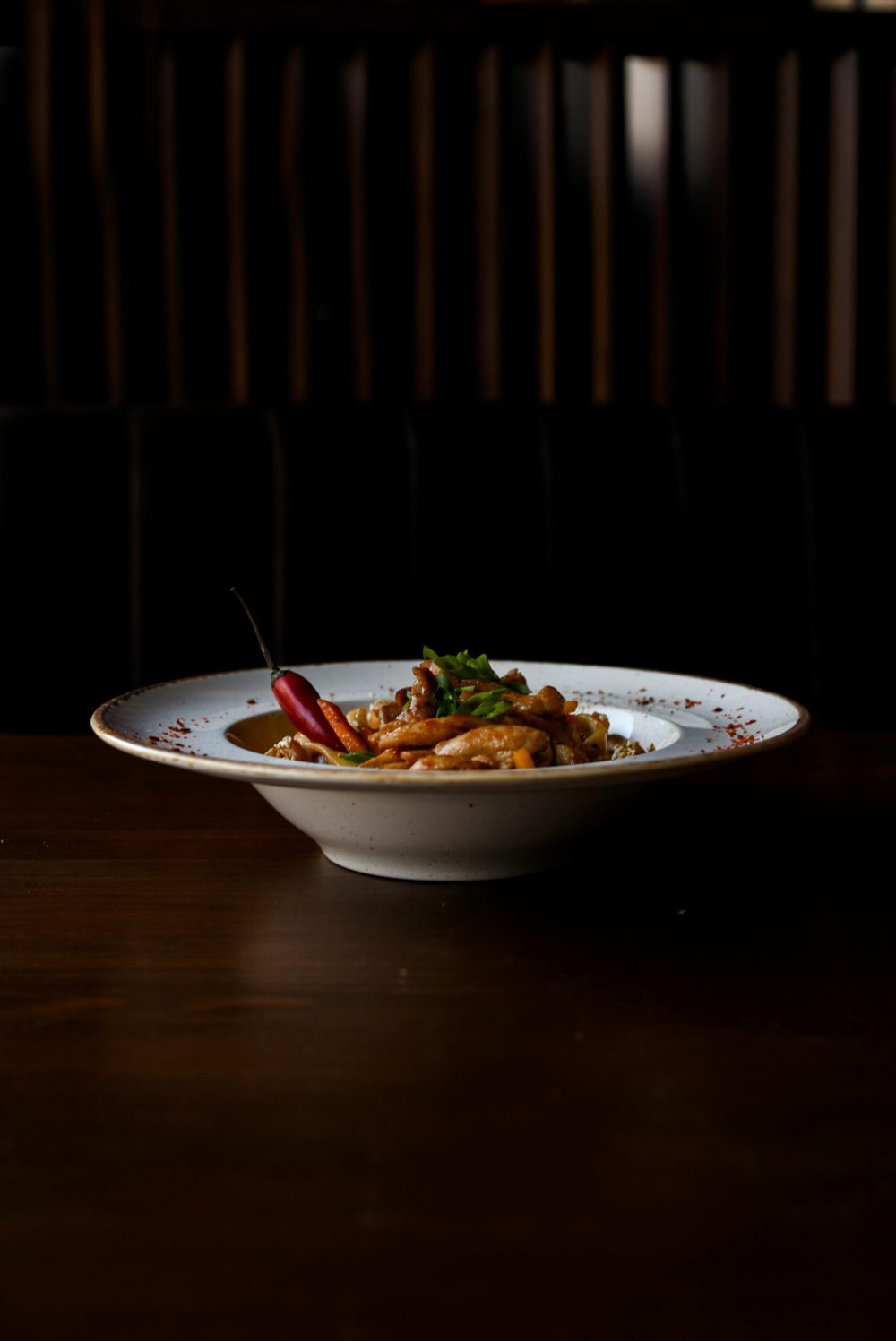 A delicious bowl of Turkish chili with red pepper garnish, captured in a moody dimly lit setting.